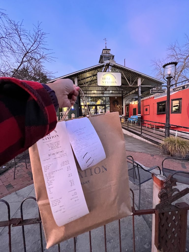 Hand holding takeout bag in front of Thai Station, ar Thai restaurant in a repurposed old train station