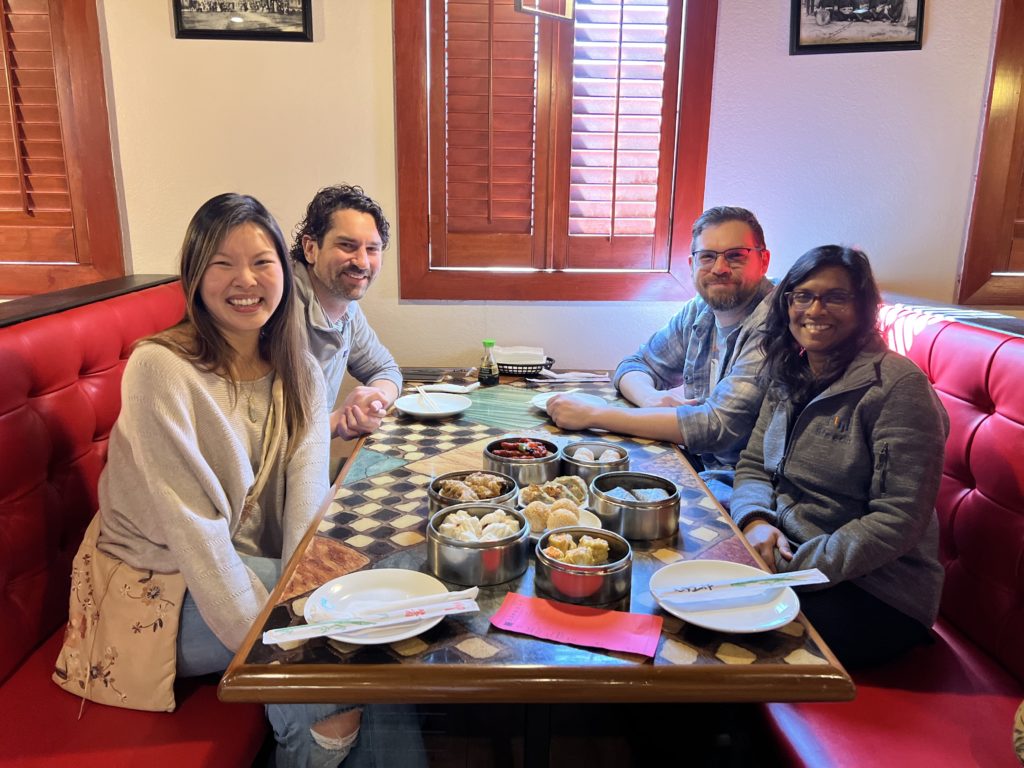 Photo of four friends sitting at a red booth inside of the restaurant with some dim sum dishes on the table. Location: Shanghai Alley in Cary, North Carolina